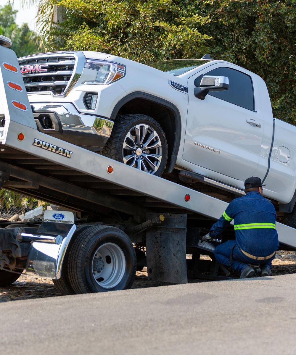 Tow truck operator loading a white pickup onto a flatbed